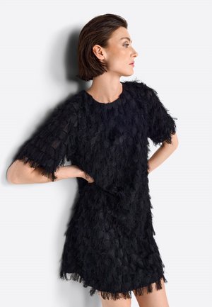 Schwarzes Kleid aus strukturiertem, gefiedertem Stoff. Kurze Ärmel, runder Halsausschnitt und lockere Passform. Akzente aus sanften, fransigen Kanten und geschichteten Details.