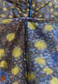 Gros plan sur un tissu avec une fermeture éclair bleue et un motif floral multicolore avec des taches jaunes, bleues et oranges sur un fond foncé.