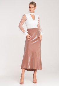 Langes Kleid mit einem weißen Oberteil, tiefem V-Ausschnitt und durchsichtigen Puffärmeln mit Punkten; fließender, glänzender Rock in Roségold mit einem subtilen Glanz.
