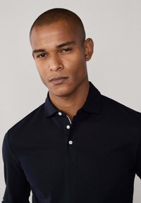 Mornarska polo majica dugih rukava s ovratnikom, tri bijela gumba i kontrastnom unutrašnjom detalj ovratnika, izrađena od glatkog pamučnog materijala.