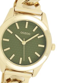 Montre en ton or avec un boîtier rond, un cadran vert texturé, des marqueurs d'heure en or et un bracelet à maillons. Présente un design minimaliste classique.