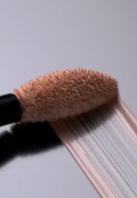 Concealerapplikator med en avsmalnande, mjuk och fluffig spets. Ljusbeige produktprovsynlig nedanför. Slät textur med en satinfinish.