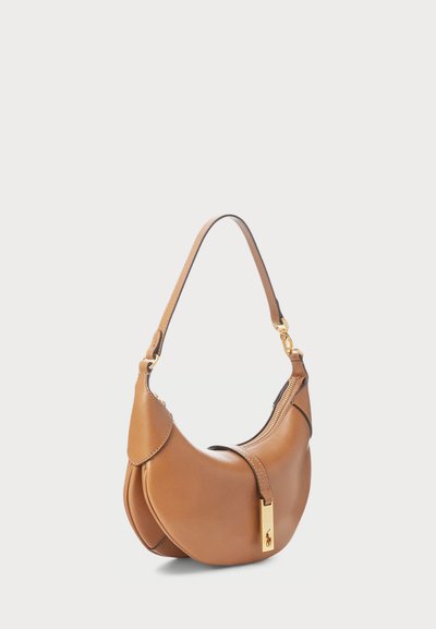 Barna bőrtáska ívelt formával, egyetlen vállpánttal, arany színű kiegészítőkkel és cipzáras záródással. Különleges oldali dizájn részlet jellemzi.