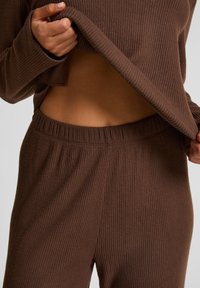 Bruine geribbelde gebreide top en bijpassende broek, met een relaxte pasvorm en zachte textuur. De top is iets gecropped, waardoor de tailleband van de broek zichtbaar is.