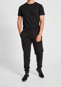 Czarny bawełniany T-shirt z krótkimi rękawami, zestawiony z czarnymi spodniami dresowymi o luźnym kroju i bocznych kieszeniach. Noszony z czarnymi butami sportowymi.