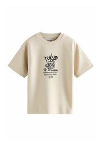 T-shirt beige a maniche corte con texture a griglia; presenta una stampa grafica nera, inclusi "TOKYO" e un design di una tigre.