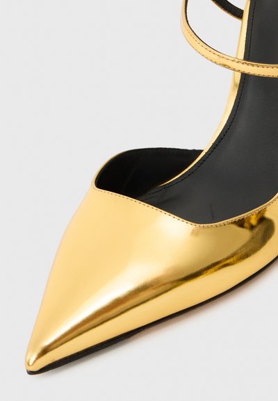 Chaussure à talon aiguille en métal doré avec un bout pointu, présentant un design découpé et de fines lanières à la cheville. Fini lisse et brillant.