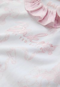 Bílá látka s bledě růžovými květinovými a motýlovými vzory, se zruffovaným výstřihem a reliéfovaným logem "Baker by Ted Baker".