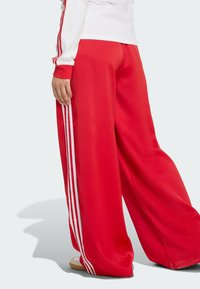 Red wide-leg pants made from smooth material with three white stripes along the sides. Finished with an elastic waistband for comfort.
