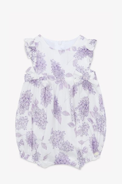 White romper with lavender floral print, featuring ruffled shoulders and bows at the waist. Soft fabric, buttons at the back and leg openings.