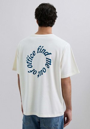 Camiseta de algodón blanca de manga corta, con texto curvado azul en la parte de atrás: "encuéntrame fuera de la oficina". Corte casual y relajado.