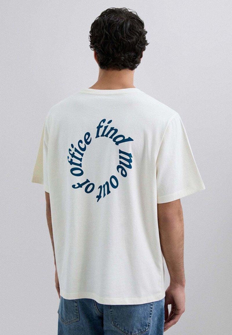 Camiseta de algodón blanca de manga corta, con texto curvado azul en la parte de atrás: "encuéntrame fuera de la oficina". Corte casual y relajado.