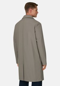 Cappotto grigio con colletto classico, taglio dritto e spacco posteriore. Materiale liscio e leggero; presenta cuciture minime per un design elegante.