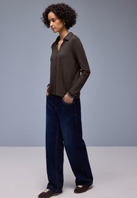 Braunes Langarmhemd mit Kragen und Knopfverschluss, kombiniert mit weitem, dunkelblauem Denim-Jeans und braunen Slippern.