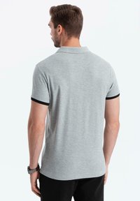 Polo grigio con rifiniture nere sulle maniche, caratterizzato da un colletto classico e maniche corte. Tessuto liscio con un design aderente.
