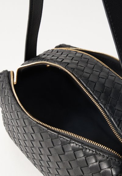 Μαύρη πλεκτή δερμάτινη τσάντα ώμου με χρυσλό φερμουάρ κατά το ήμισυ ανοιχτό, που δείχνει το άδειο εσωτερικό.