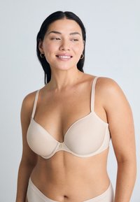Beige bh met gladde cups, verstelbare schouderbanden en een centrale haak. Zachte stoftextuur met minimale details.