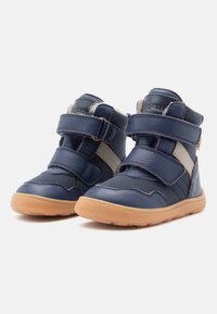 Baskets montantes en cuir bleu marine avec deux bandes Velcro, un accent beige et une semelle en caoutchouc ; caractéristiques en matériau texturé pour le confort.