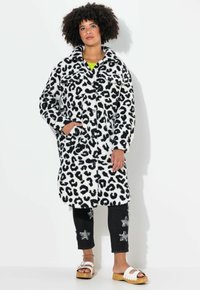 Lederjakke i leopardprint i sort og hvidt imiteret pels med to forlommer og krave, parret med mørke jeans med stjernemønstre og hvide sandaler.
