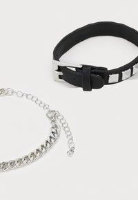 Bracelet en cuir noir avec des clous en argent et bracelet en chaîne argentée avec un fermoir ajustable. Les deux accessoires ont une texture lisse.