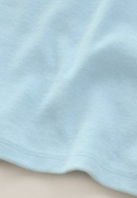 Helltblauer Baumwollstoff mit weicher Textur, der glatte Kanten und leichte Falten aufweist und ein schlichtes, einheitliches Design zeigt.