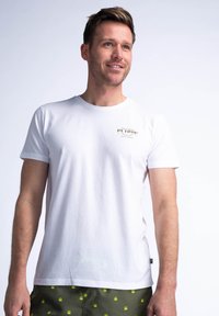 Bílé bavlněné tričko s kulatým výstřihem a krátkým rukávem. Obsahuje malé tištěné logo ve zlaté barvě na levé části hrudníku.
