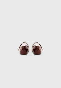 Brown patent leather ballet flats with a narrow strap and buckle detail at the back, flat soles and rounded toe design.