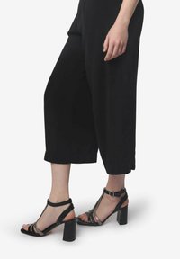 Zwarte cropped broek gecombineerd met zwart en grijs hoge sandalen met meerdere banden, een blokhak en een verstelbare enkelgesp.