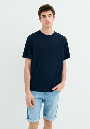 Camiseta de rayas azul marino con mangas cortas, escote redondo y corte relajado, combinada con pantalones cortos de mezclilla azul claro con puños doblados.