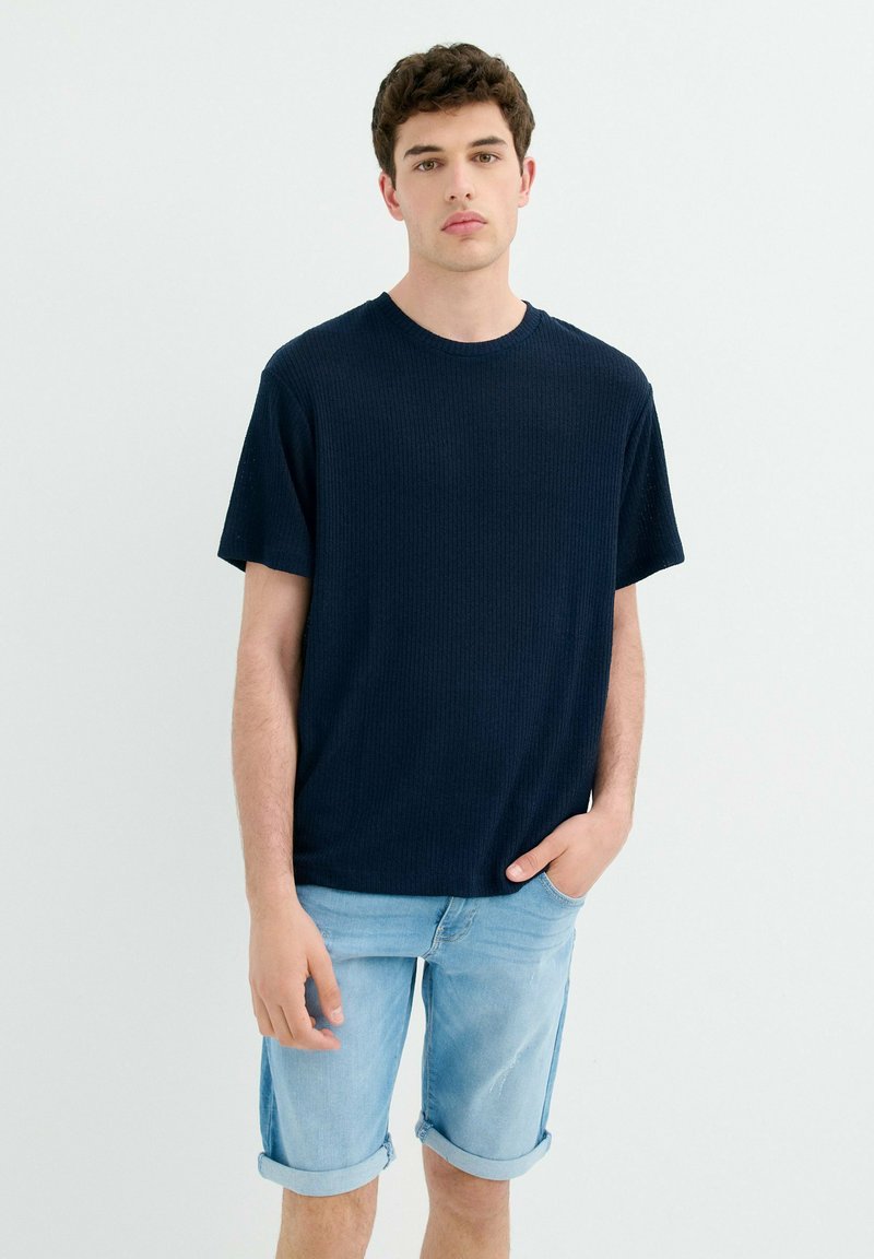 Camiseta de rayas azul marino con mangas cortas, escote redondo y corte relajado, combinada con pantalones cortos de mezclilla azul claro con puños doblados.