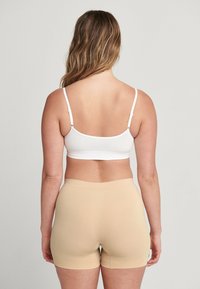 Witte geribbelde bralette met verstelbare bandjes, gecombineerd met naadloze beige shorts. Soepele textuur en aangesloten ontwerp, geen zichtbare naden of patronen.