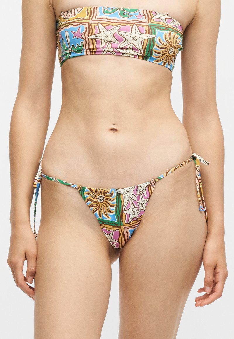 Femme portant un haut de bikini bandeau et un bas de bikini à nouer sur les côtés avec des motifs colorés de vie marine, incluant des étoiles de mer et des coquillages.