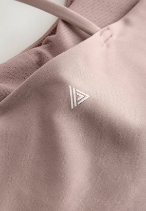 Gaiši rozā sporta krekls bez piedurknēm ar mīkstu tekstūru, kamēr tas ir elpojošs ar acs dizainu un auduma mazs trīsstūrveida logotips.