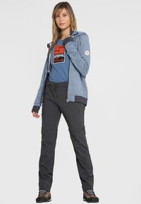 Sudadera azul con cremallera y detalles en gris, combinada con pantalones gris oscuro. El conjunto incluye un logo en la camiseta y calzado resistente.