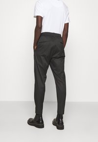 Svarta rutiga byxor med resårmidja, avsmalnande ben och sidofickor, i kombination med en enkel vit T-shirt och svarta skor.