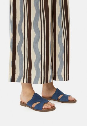 Modré semišové sandále na klíne s dizajnom prekrižovaných popruhov a otvorenou špičkou, skombinované s pruhovanými širokými nohavicami v hnedých a modrých odtieňoch.