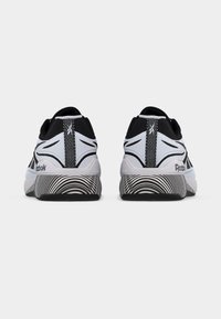 Ζευγάρι ασπρόμαυρα αθλητικά παπούτσια Reebok, εμφανιζόμενα από πίσω, με μοτίβο στη μέση της σόλας και θηλιές τραβήγματος με λευκό λογότυπο.