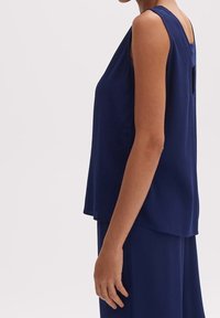 Granatowa, bezrękawnikowa bluzka o luźnym kroju, okrągłym dekolcie i wycięciu na plecach. Wykonana z gładkiego materiału, bez widocznych wzorów i dodatków.