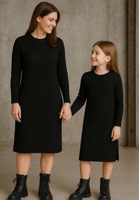 Schwarze, gerippte Strickkleider mit langen Ärmeln und Rundhalsausschnitten. Beide kombiniert mit schwarzen Schnürstiefeln, stehen zusammen und halten Händchen.