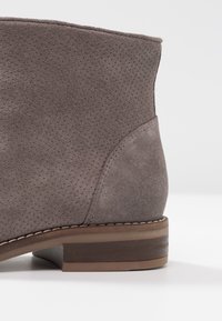 Gray suede ankle boot with perforated texture, flat brown heel, and stitched accents at the sole and heel.