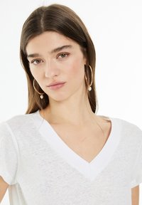 White, lightweight v-neck t-shirt with short sleeves, featuring a subtle texture. Model wears gold hoop earrings with pearl accents.
