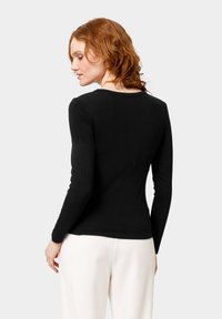 Zwart langemouwtop met een ronde halslijn, geribbelde textuur en een aansluitend ontwerp, gecombineerd met lichtgekleurde broek, gezien vanuit de achterkant.