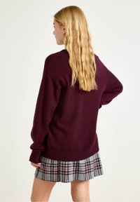 Burgundy tröja i mjukt stickat med sänkta axlar, kombinerad med en grå rutmönstrad plisserad kjol med vinröda accenter.