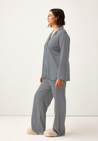 Pigiama a righe in blu e bianco, composto da una maglietta con bottoni, maniche lunghe e pantaloni larghi, abbinato a pantofole beige soffici.