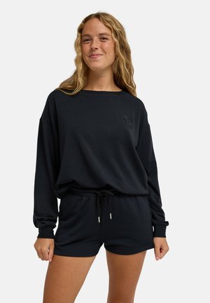 Sort sweatshirt med lange ærmer og rund halsudskæring, kombineret med sorte shorts med elastik i taljen og snører.