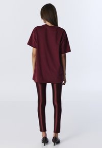 Bordowy, oversize t-shirt z krótkim rękawem, w połączeniu z błyszczącymi bordowymi legginsami, uzupełniony o czarne szpilki w kształcie szpica. Gładka tekstura.