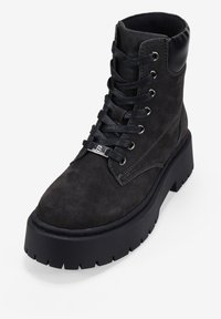 Stivaletto alla caviglia in suede nero con punta arrotondata, design con lacci, occhielli in metallo e suola piatta nera in gomma spessa. Presenta dettagli in pelle nera liscia.