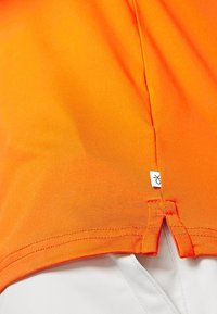 Camisa naranja de manga corta hecha de tejido suave, con una sutil textura acanalada, con una abertura en el dobladillo en la parte trasera y una pequeña etiqueta de logo.