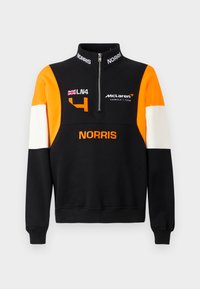 Musta huppari korkealla kauluksella ja vetoketjulla, jossa on oranssit ja valkoiset hihat. Näyttää sanat "McLaren," "LN4," ja "NORRIS" kontrastiväreissä.