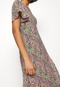 Blumenkleid mit schwarzem Grundton und Mustern in Pink, Grün und Gelb, kurzen, schwingenden Ärmeln und einer fließenden Silhouette.
